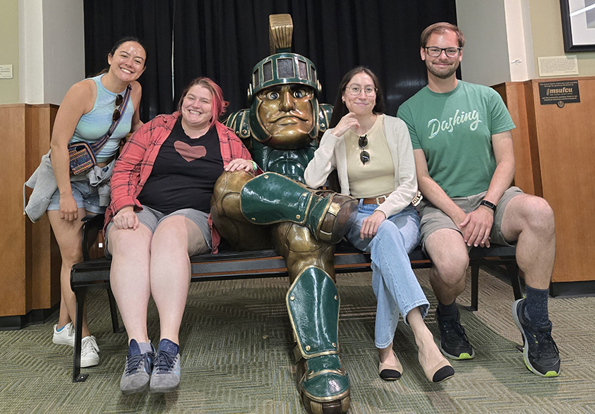 Photograph of students and faculty sitting near a Spartan statue at Michigan State University.