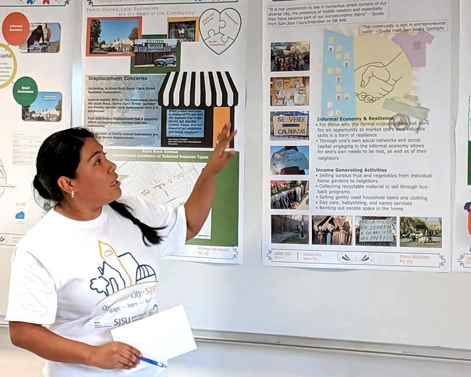 A Masters student in Urban Planning stands in front of research posters presenting to community members